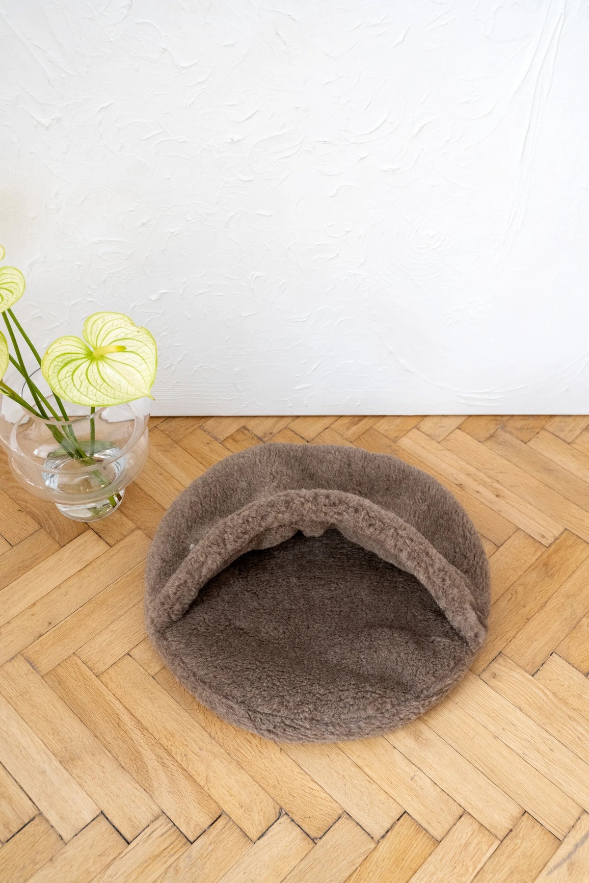 Natural Wool Pet Cave - Beige, Cozy Pet Bed on a wooden floor with a plant in the background.
